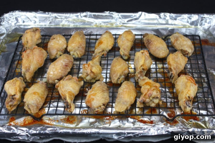 Baked chicken wings tossed with buffalo sauce on a wire rack on a foil lined baking sheet.