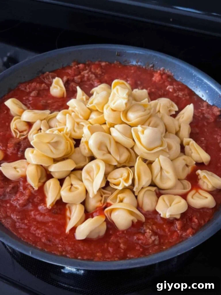 Tortellini added to the creamy tomato and sausage sauce in a skillet, ready to cook.