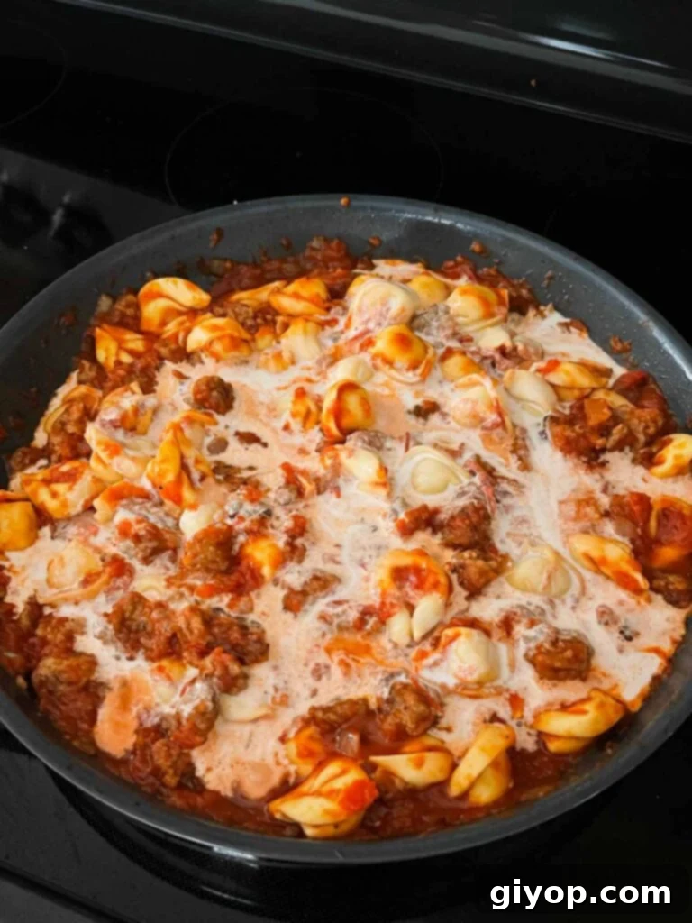 Heavy cream being stirred into the tortellini with Italian sausage and tomato sauce.