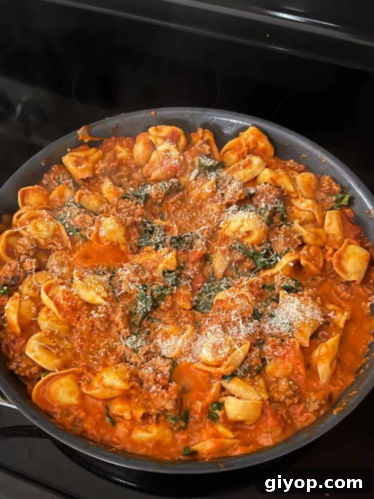 Grated cheese being sprinkled over the finished one-pot tortellini with Italian sausage and spinach.