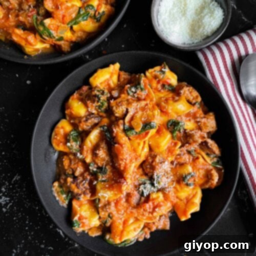 Tortellini with Italian sausage and spinach in a dark bowl on a dark surface.