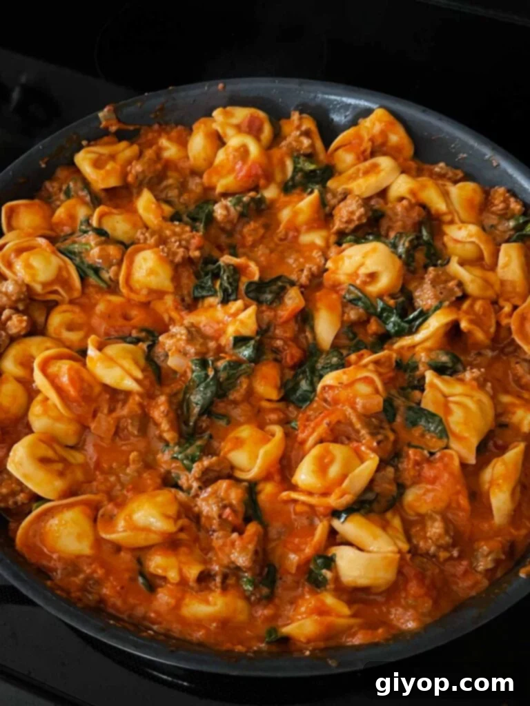 Close-up of a skillet filled with cooked tortellini, Italian sausage, and spinach in a creamy tomato sauce.
