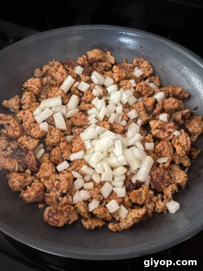 Diced onions added to the browned Italian sausage in a hot skillet, beginning to soften.