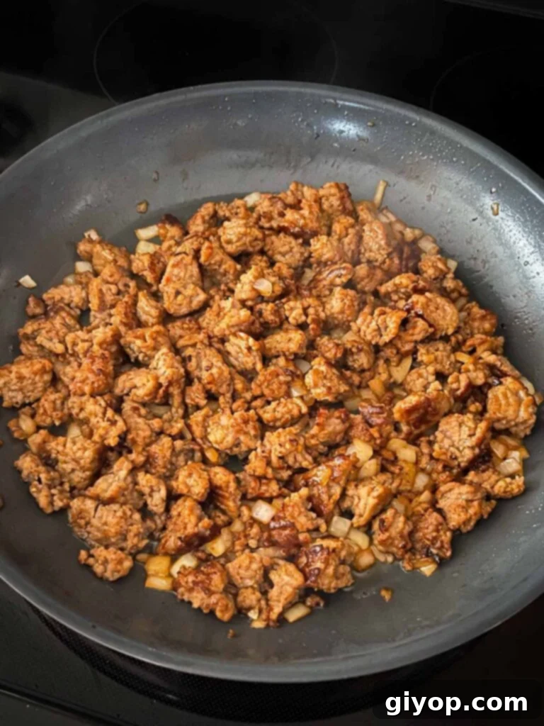 Cooked Italian sausage and translucent onions simmering in a skillet.