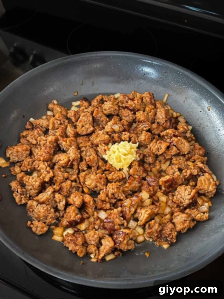 Minced garlic added to the cooked Italian sausage and onions in a skillet, filling the air with aroma.