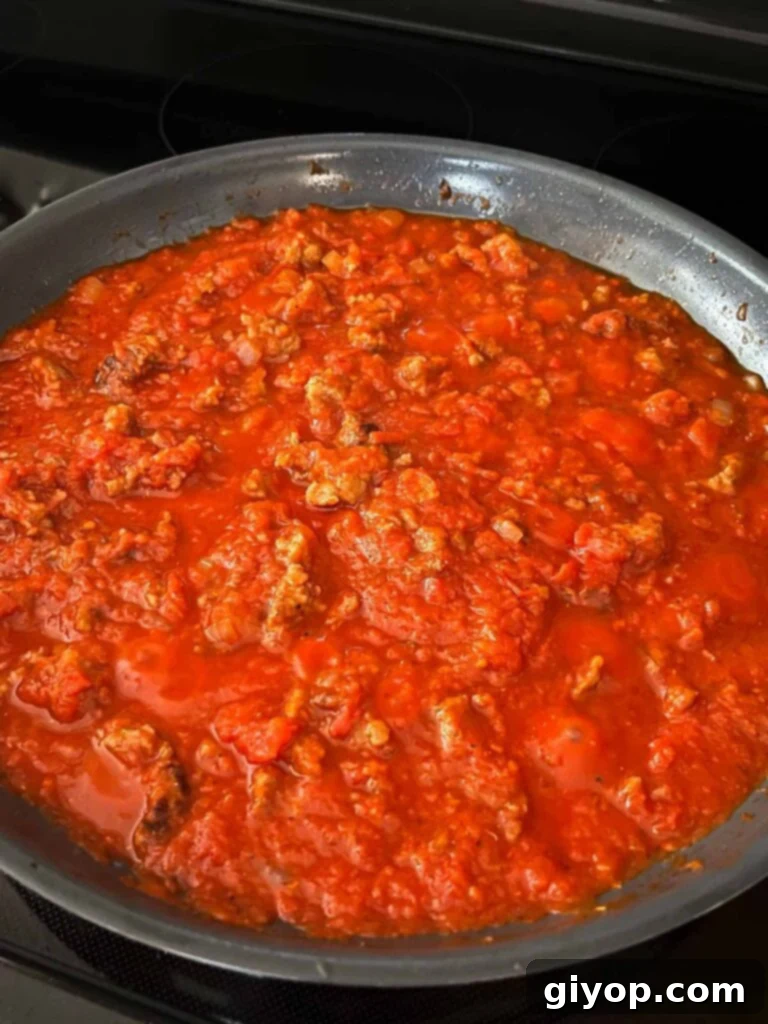 Rich tomato sauce with Italian sausage simmering gently in a skillet, flavors deepening.
