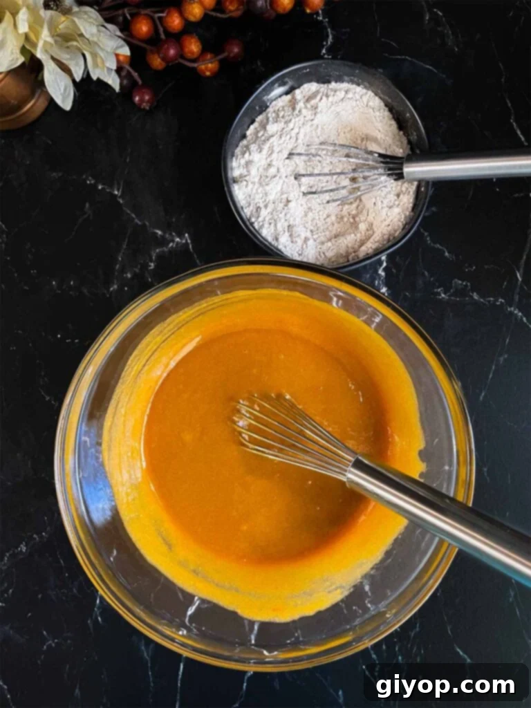 Combined wet ingredients for sweet potato muffins in a large glass bowl on a dark surface.