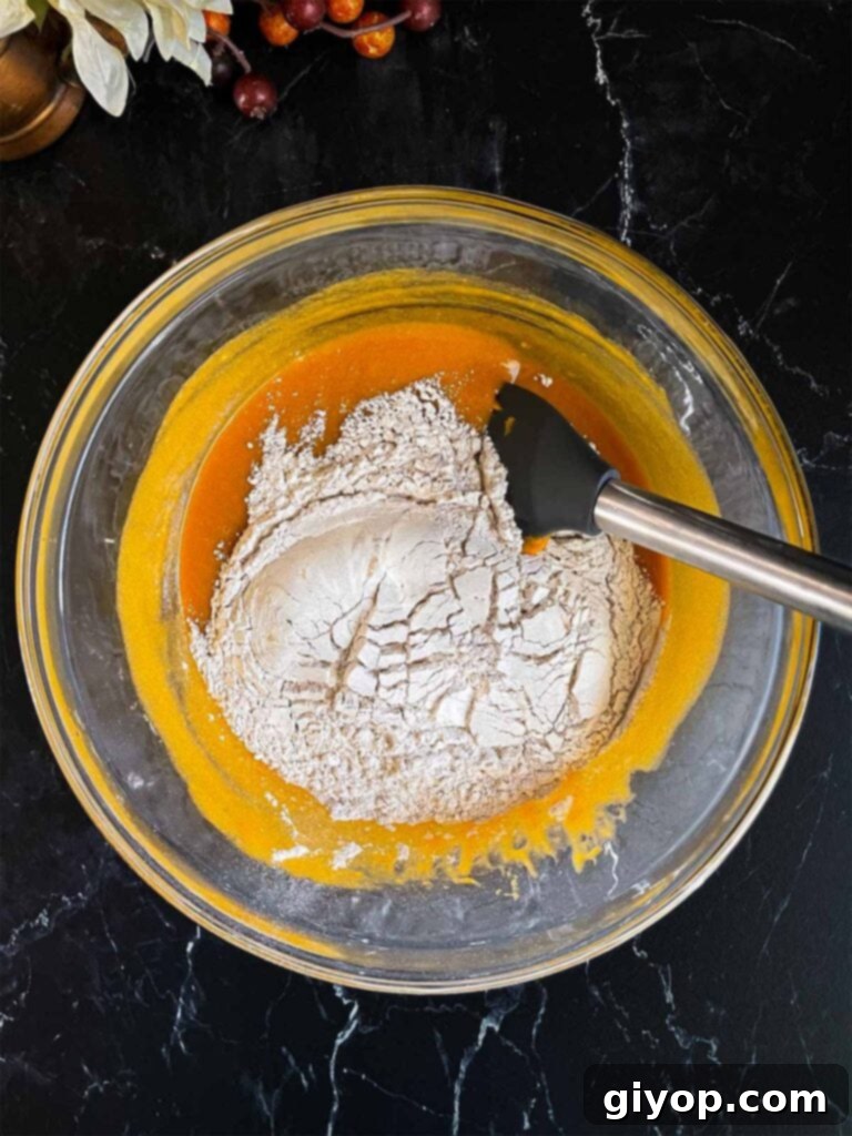 The dry ingredients added to the wet ingredients in a large glass bowl for sweet potato muffins.