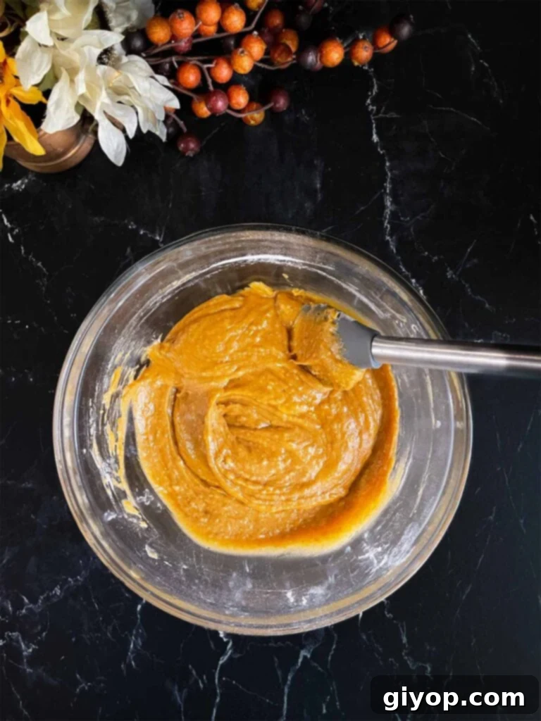 Sweet potato muffins batter mixed in a large glass bowl on a dark surface.