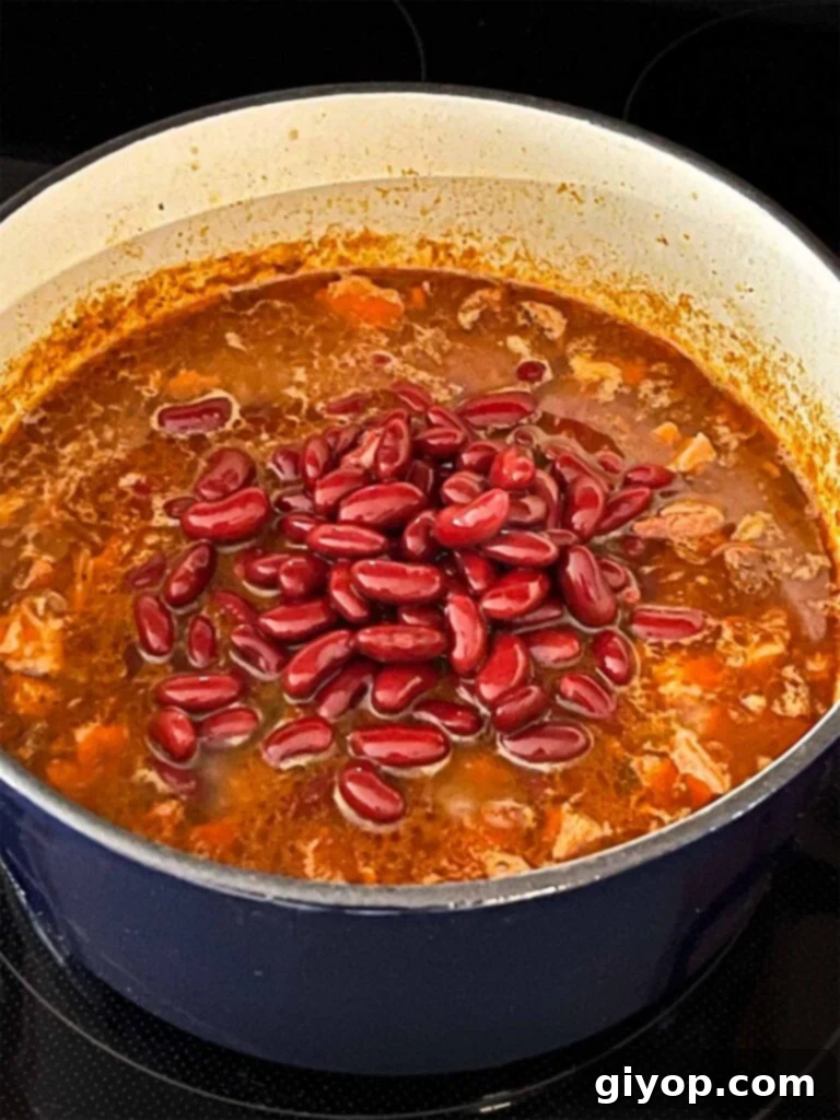 Adding pinto beans to smoked pork chili in a dutch oven.
