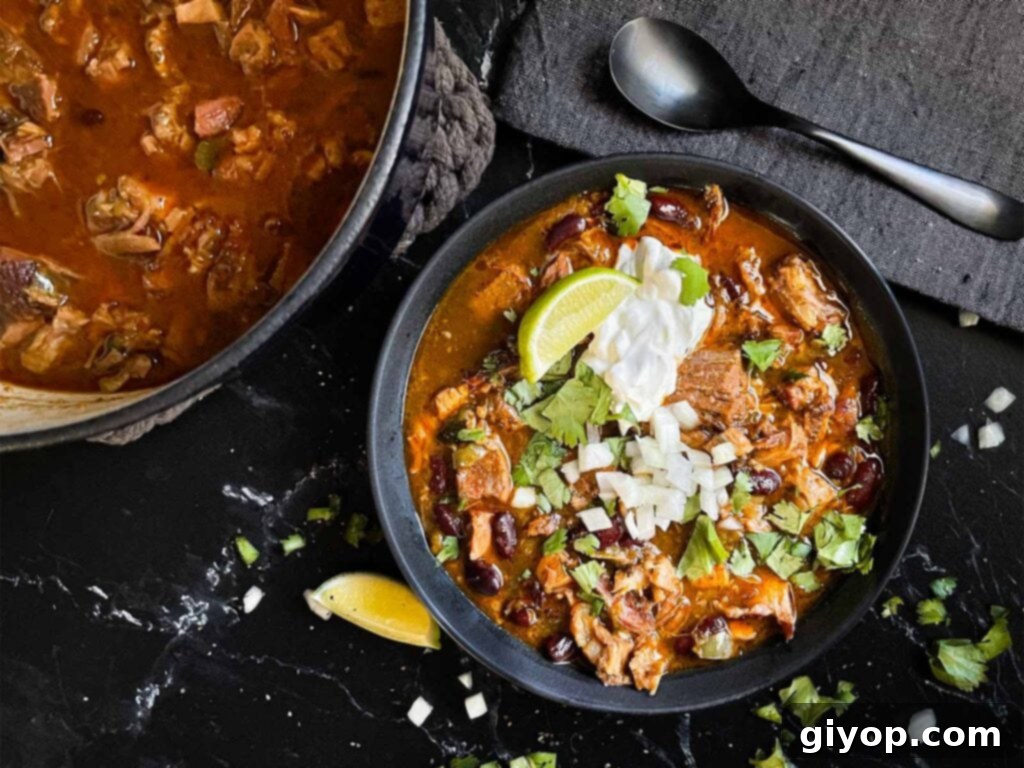 Smoked pork chili garnished with cilantro, onion, lime, sour cream, and onion in a dark bowl.