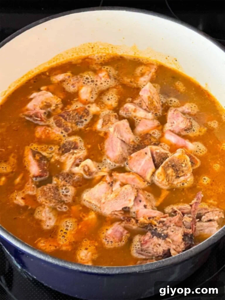 Smoked pork added to chili base in a dutch oven.