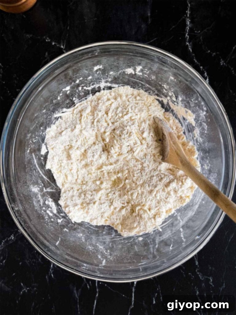 The grated butter tossed with the flour mixture for sweet potato biscuits in a glass bowl on a dark surface.