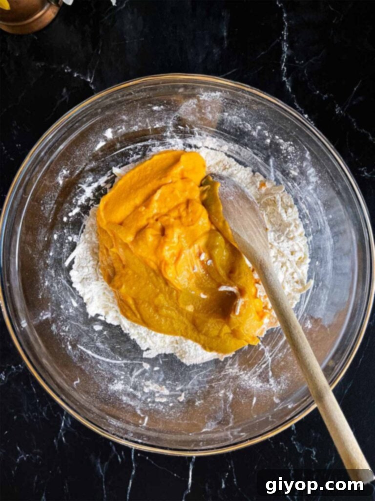 Sweet potato mixture added to the flour and butter mixture for sweet potato biscuits in a glass mixing bowl on a dark surface.