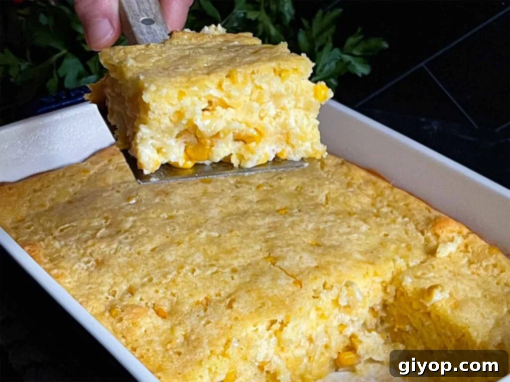 A serving of creamy corn casserole lifted over the baking pan on a dark surface.