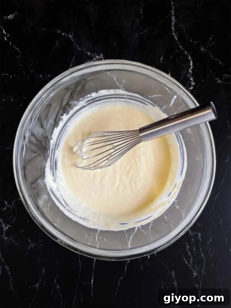 Corn casserole wet ingredients whisked together in a glass mixing bowl.