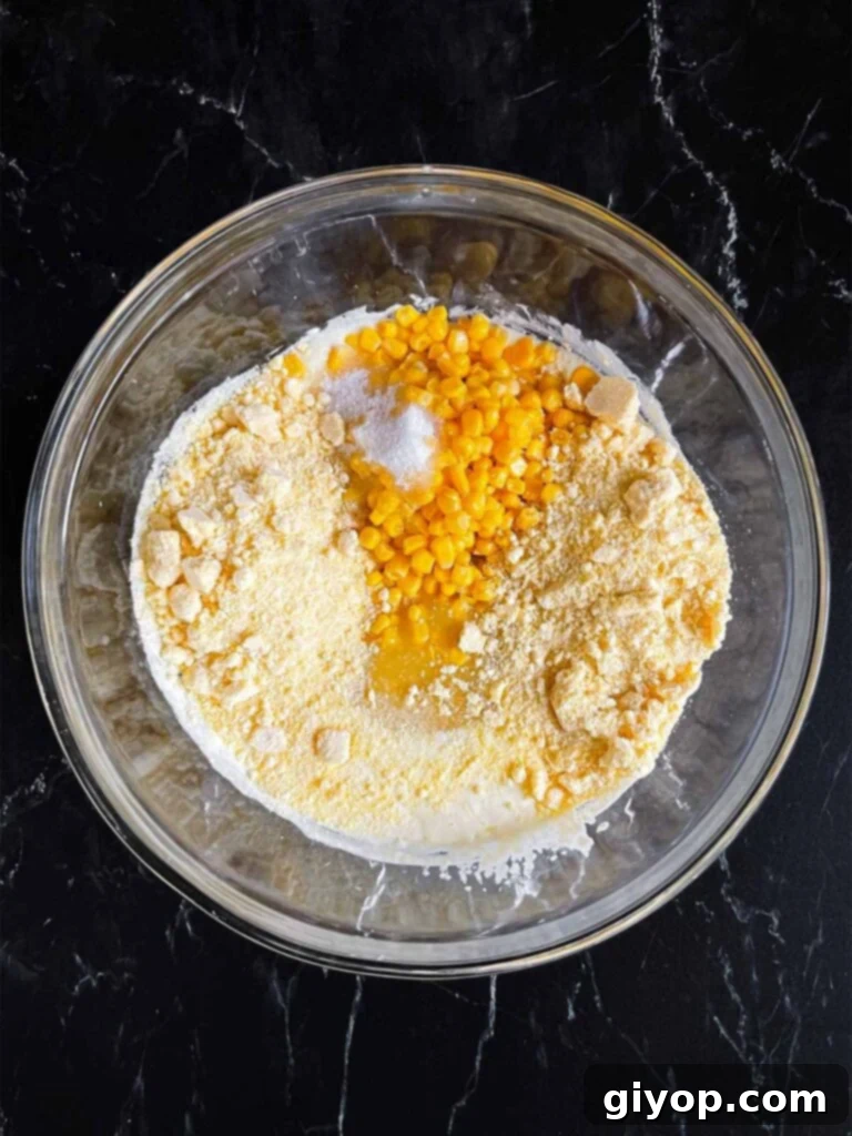 Corn and dry ingredients added to the wet ingredients in a glass bowl.