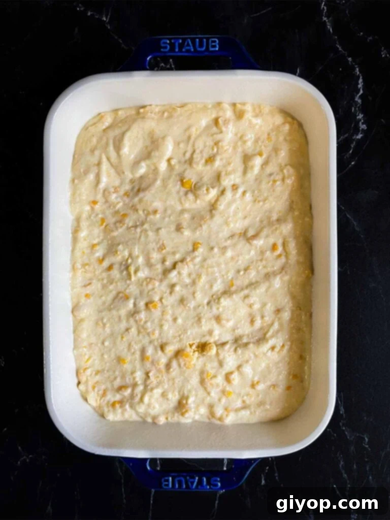 Corn casserole batter in a baking pan on a dark surface.
