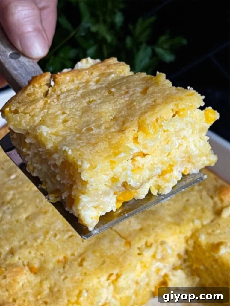 A serving of creamy corn casserole lifted over the baking pan on a dark surface.