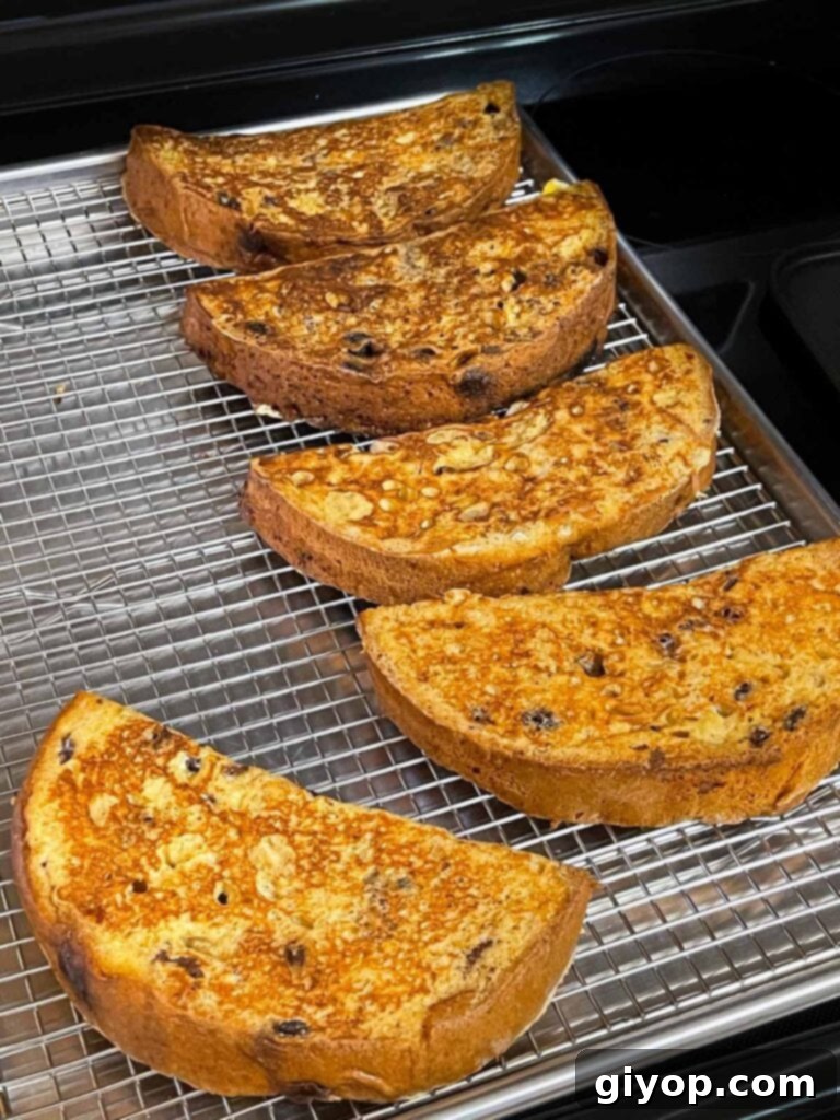 Cooked panettone French toast slices resting on a wire rack lined baking sheet, keeping warm and crisp in the oven.
