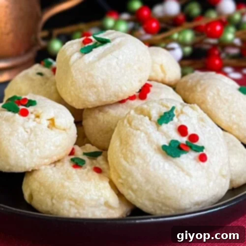 Whipped shortbread cookies stacked on a dark plate.