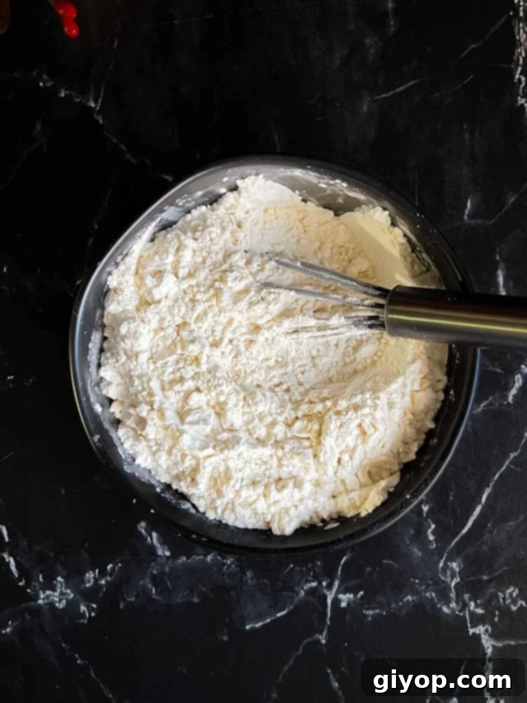 All-purpose flour, cornstarch, and kosher salt whisked together in a dark bowl, preparing the dry mixture for baking.