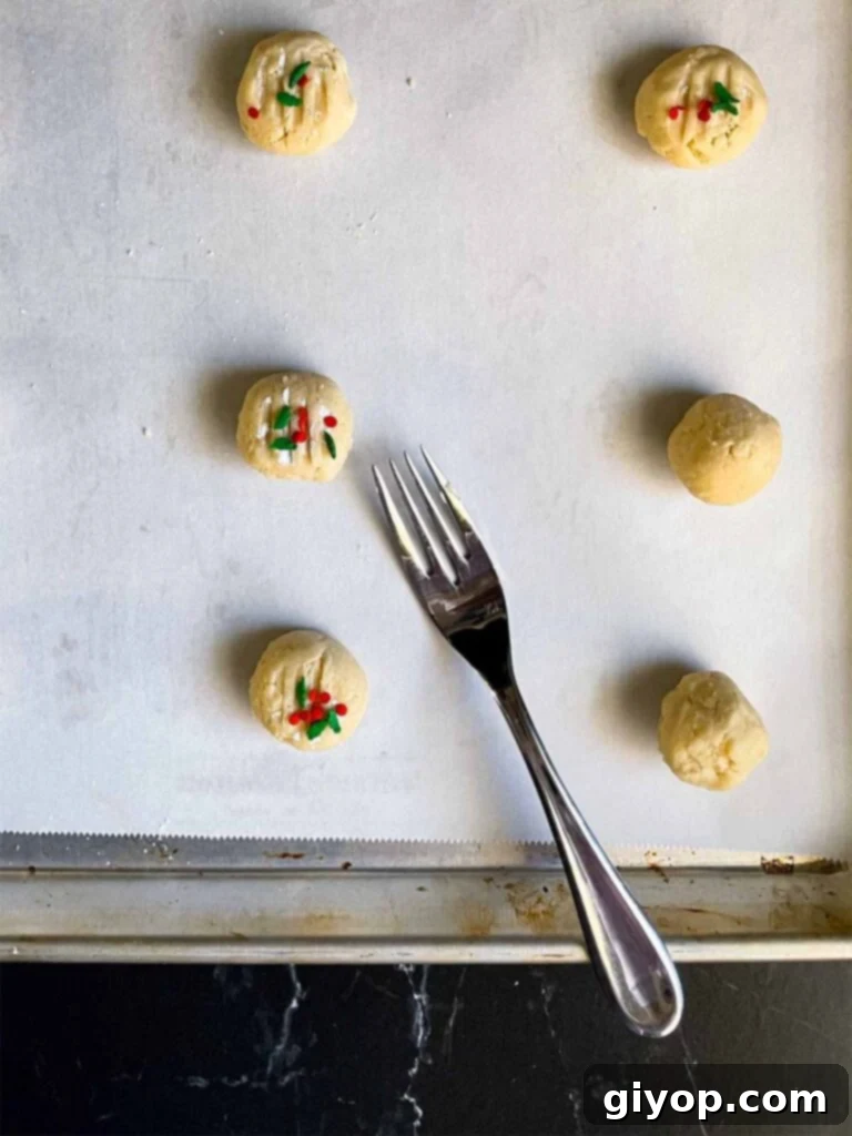 Neatly formed whipped shortbread cookie dough balls, gently pressed with a fork, arranged on a parchment paper-lined baking sheet.