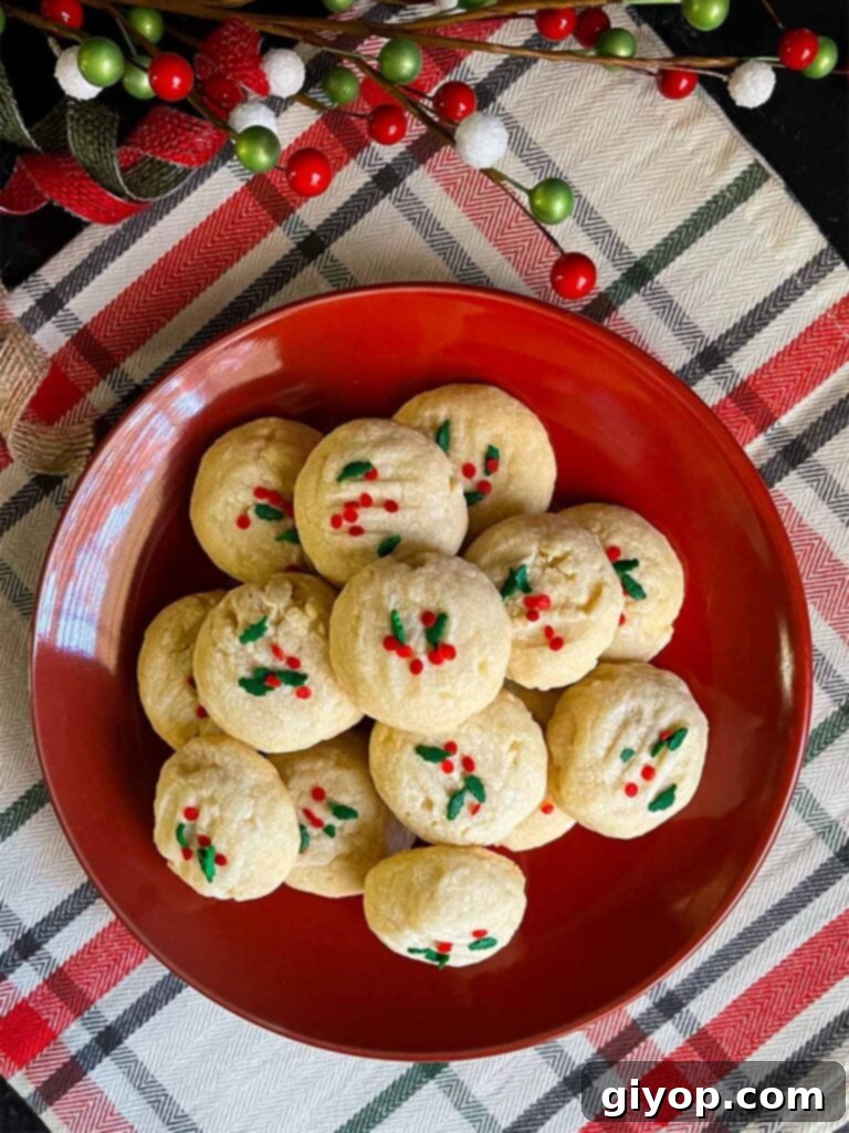 A beautiful stack of freshly baked, golden-edged whipped shortbread cookies, garnished with sprinkles, on a dark plate.
