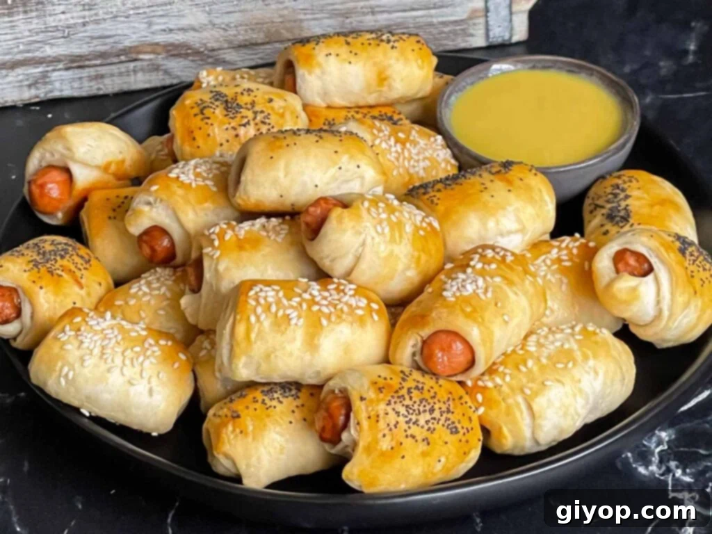 Pigs in Fluffy Biscuits 2 Pigs in a blanket stacked on a dark plate with a ramekin of honey mustard sauce.