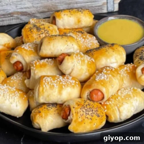 Pigs in Fluffy Biscuits 9 Pigs in a blanket stacked on a dark plate with a ramekin of honey mustard sauce.