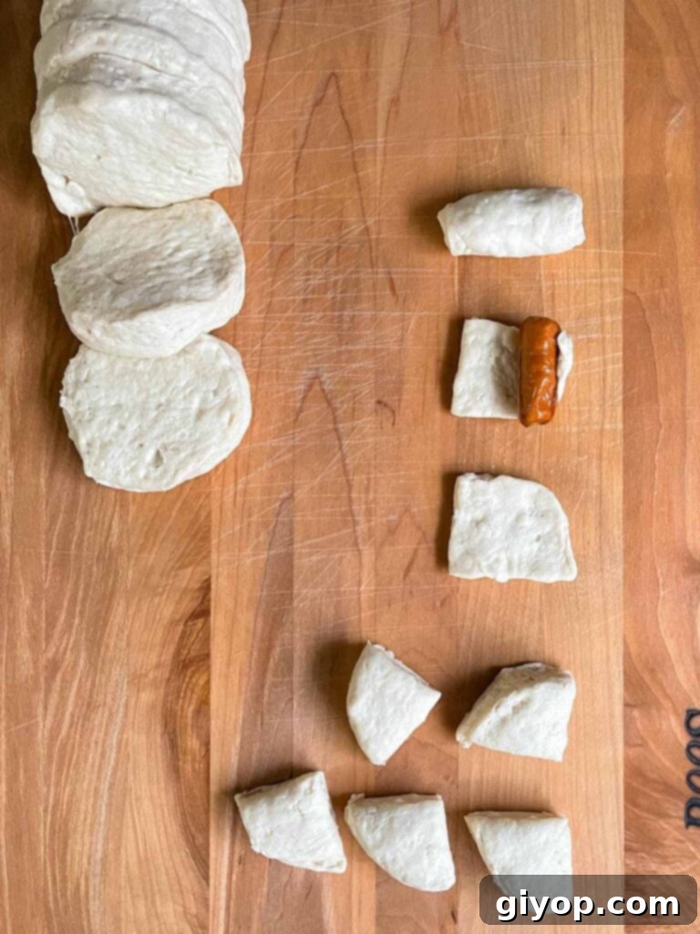 Pigs in Fluffy Biscuits 6 Biscuit dough cut into quarters and being wrapped around a cocktail smokie sausage.