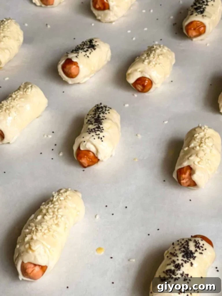 Pigs in Fluffy Biscuits 7 Unbaked pigs in a blanket on a parchment paper lined baking sheet.
