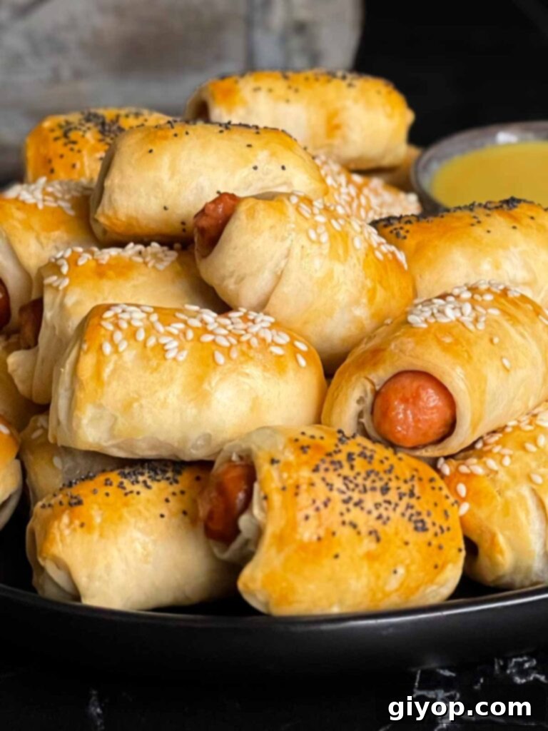 Pigs in Fluffy Biscuits 8 Pigs in a blanket stacked on a dark plate with a ramekin of honey mustard sauce.