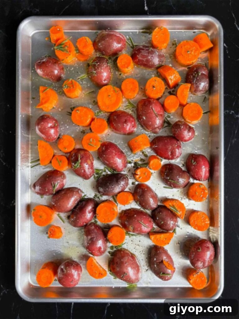 Seasoned potatoes and carrots spread evenly in a single layer on a baking sheet, ready for the oven.