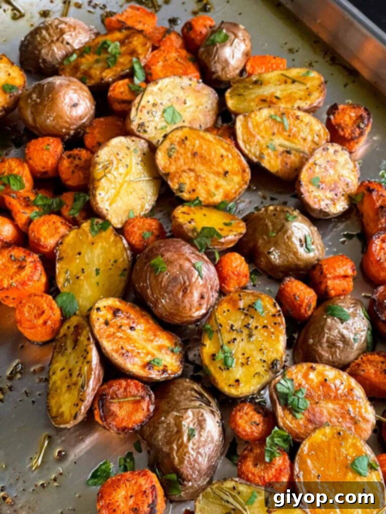 Freshly roasted potatoes and carrots on a baking sheet, glistening and golden.