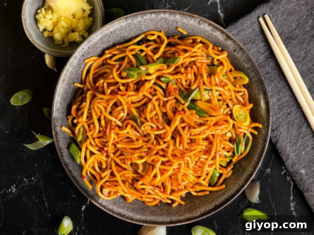 Spicy garlic noodles in a dark bowl, garnished with green onions.