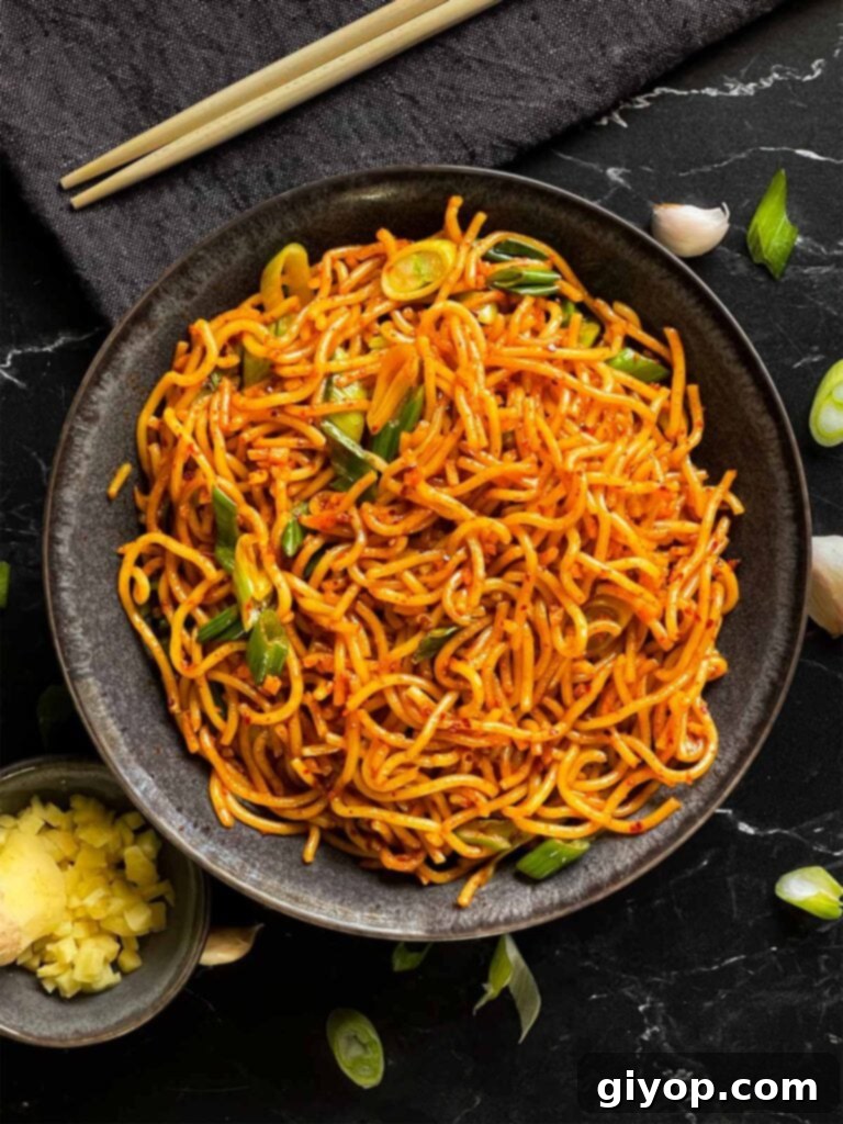 Close-up of spicy garlic noodles in a dark bowl, showing texture and garnishes.