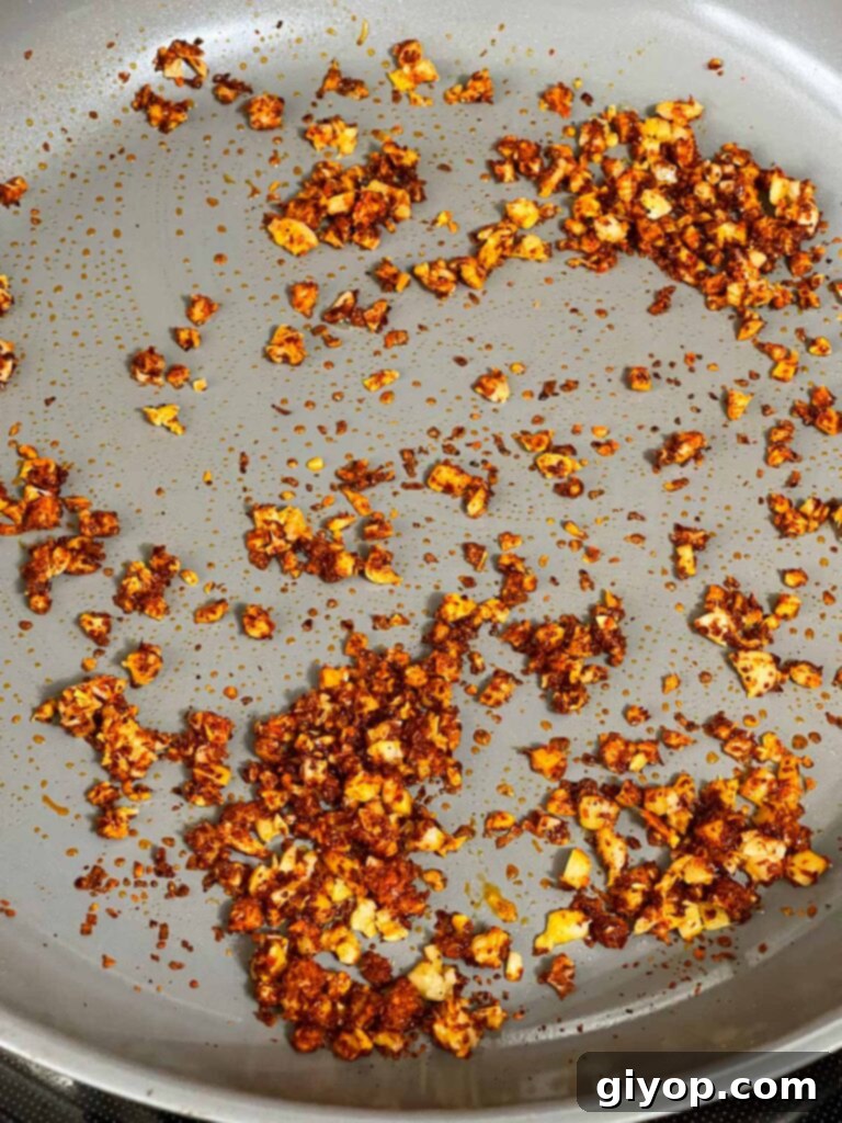 Gochugaru spice being added to a skillet with ginger and garlic.