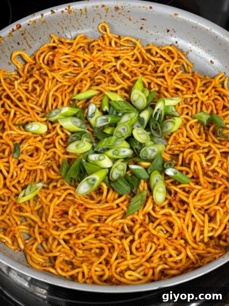 Adding sliced green onions to the noodle dish in a skillet.