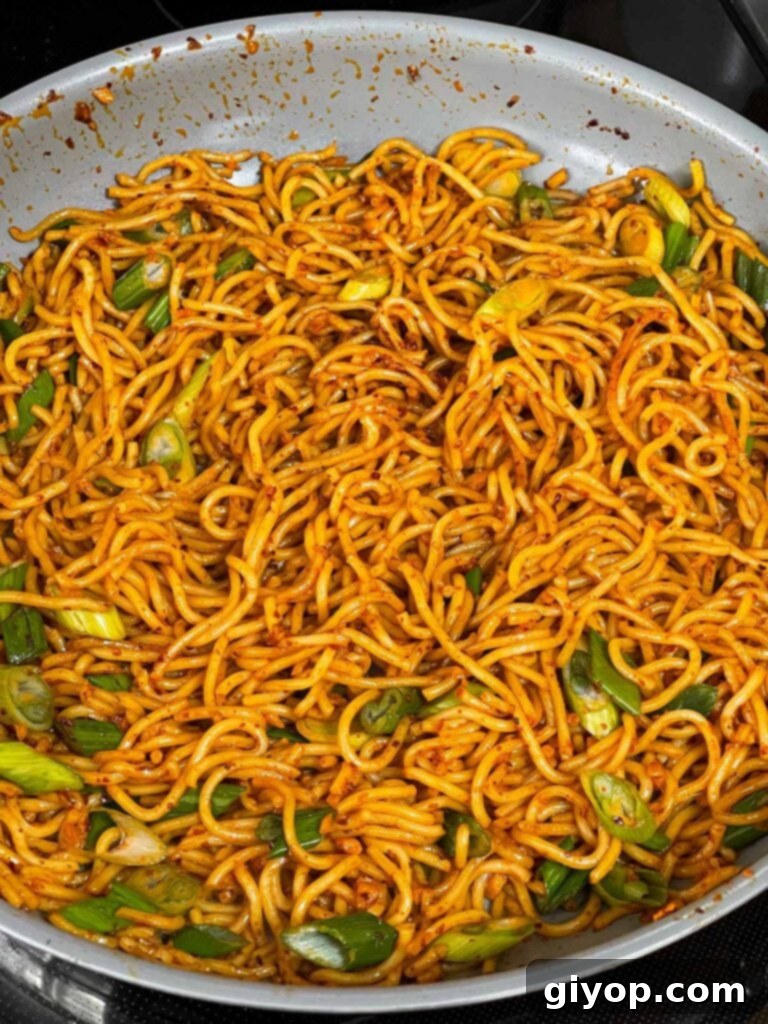 Spicy garlic noodles being tossed in a skillet, coated in sauce.