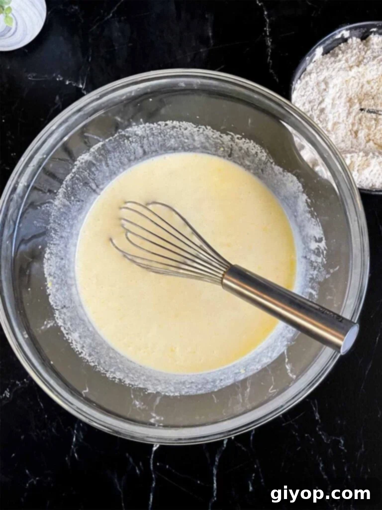 Wet ingredients for lemon poppy seed muffins, including buttermilk, oil, and lemon extract, whisked together in a glass mixing bowl, poised for combination with dry ingredients.