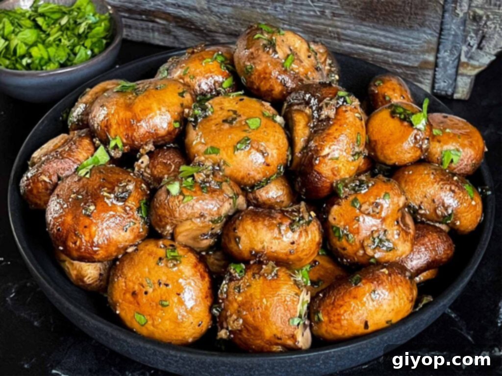 Garlic butter roasted mushrooms in a dark bowl on a dark surface.