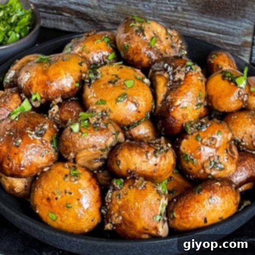 Garlic butter roasted mushrooms in a dark bowl on a dark surface.