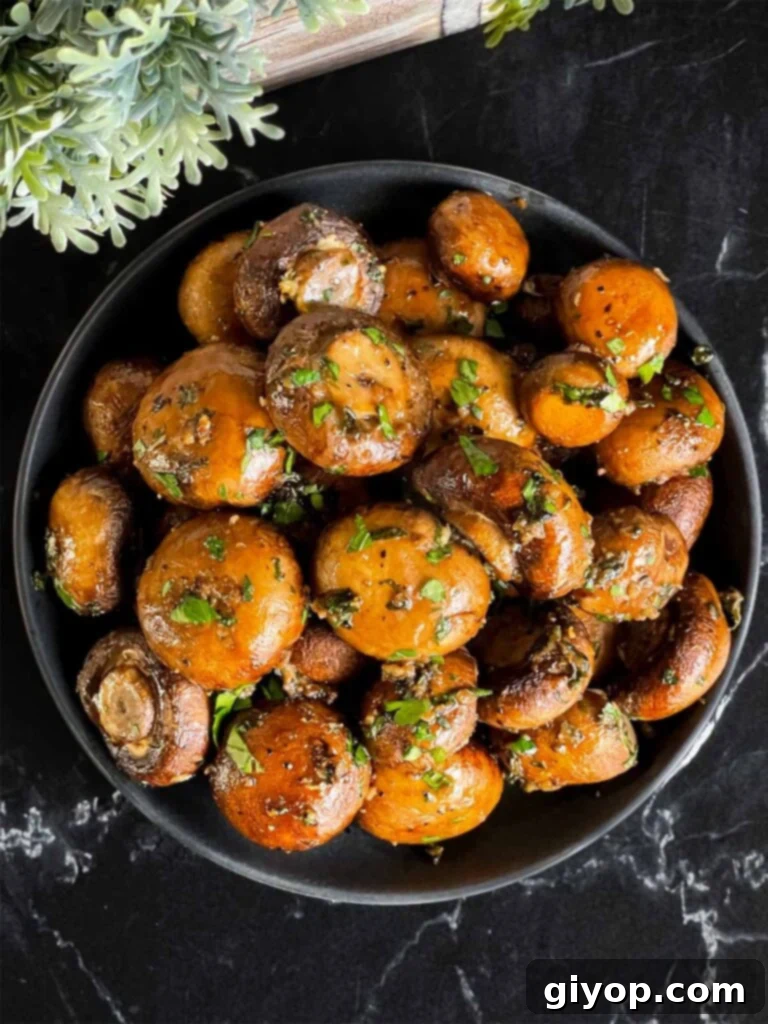 Garlic butter roasted mushrooms in a dark bowl on a dark surface.