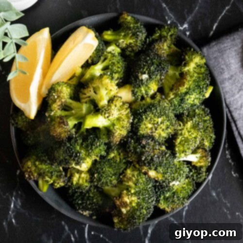 Crispy Roasted Broccoli 8 Roasted broccoli with lemon wedge garnish in a dark bowl.