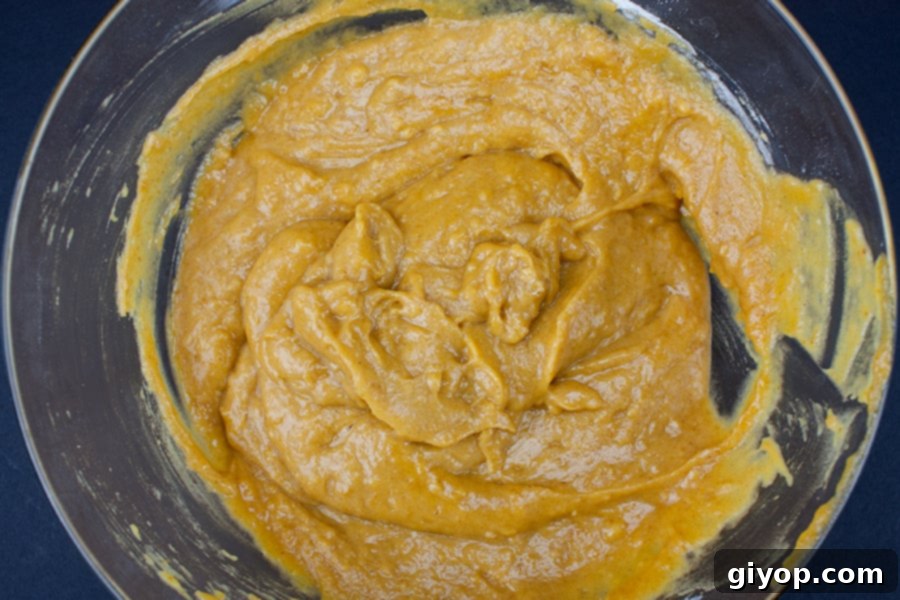 The smoothly whisked wet ingredient batter for bakery-style pumpkin muffins, showcasing its rich, creamy texture in a clear glass mixing bowl.