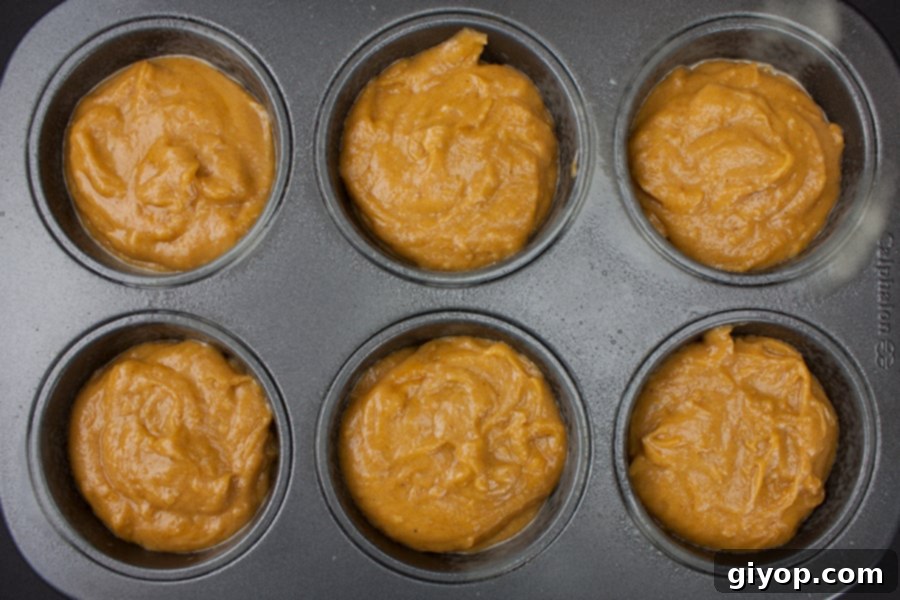Jumbo muffin tin filled with raw pumpkin muffin batter, ready for baking, promising large, fluffy treats.