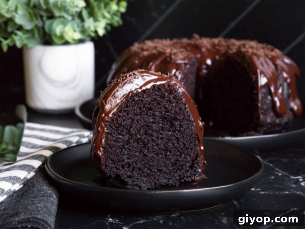 A beautifully sliced moist chocolate bundt cake, showing its rich, dark crumb, on a dark plate, drizzled with glossy chocolate ganache.