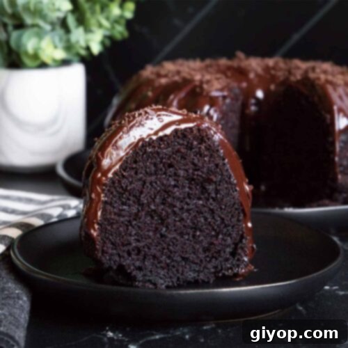 A slice of chocolate bundt cake on a dark plate, showing its interior and ganache.