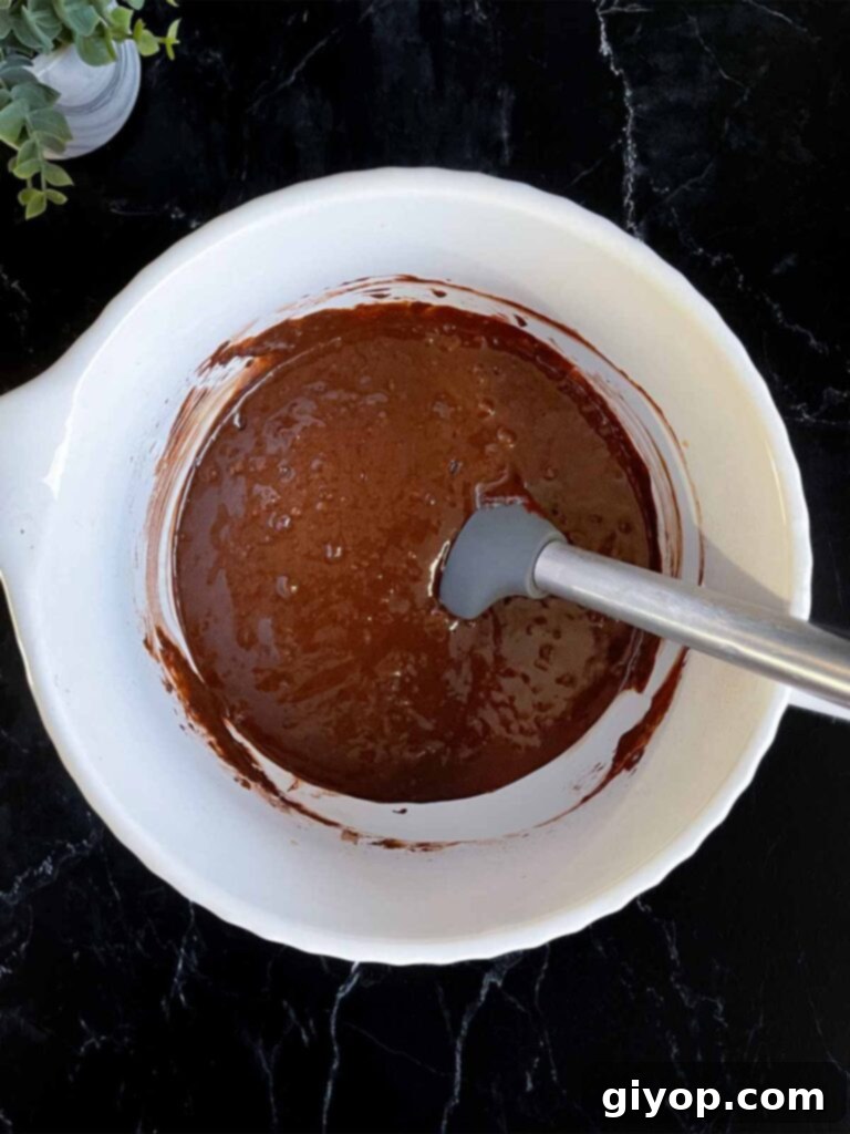 Smooth chocolate bundt cake batter ready for baking in a large mixing bowl on a dark surface.